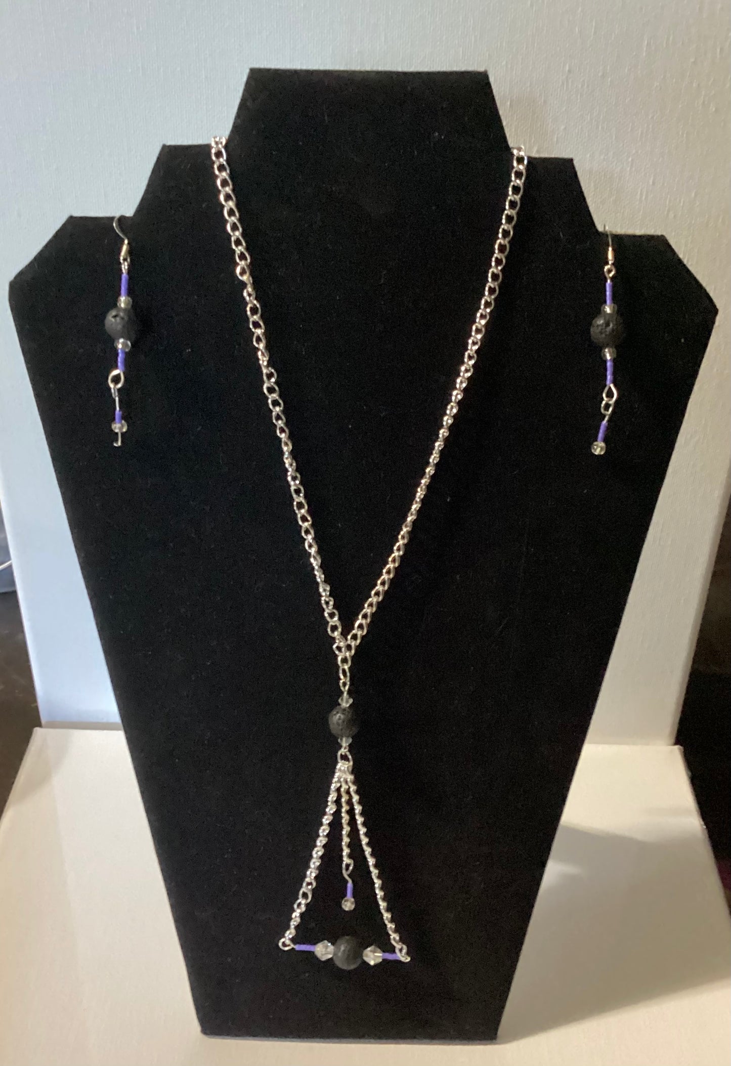 Necklace and earrings set on a black display stand with a white background