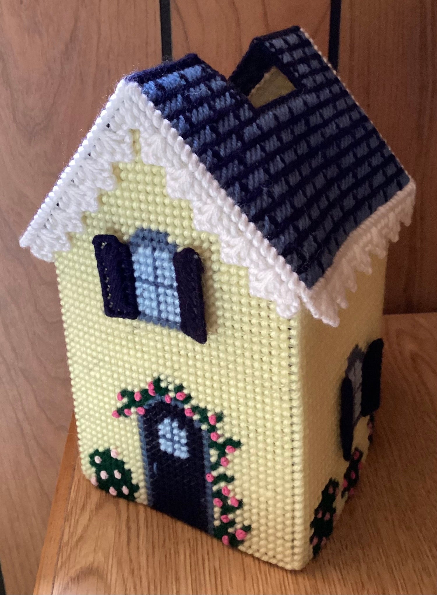 Cottage plastic canvas tissue box cover.  Yellow cottage with white trimmed blue roof.  Blue windows and doors trimmed by pink flowers and bushes.